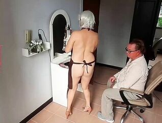 Naturist barbershop. Bare chick hairdresser in an apron